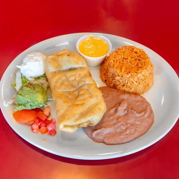 A fried burrito with rice, refried beans, guacamole, sour cream, and diced tomatoes on a white plate.