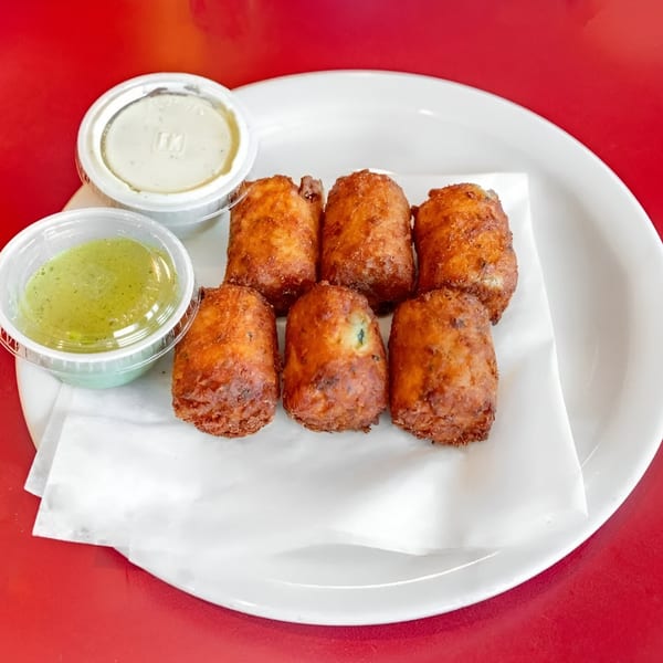 Six golden-brown fried Mexican appetizers on a white plate with two dipping sauces.