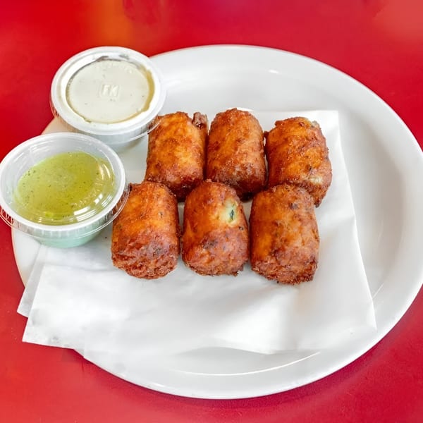 Six golden-brown fried Mexican croquettes with two dipping sauces on a white plate.