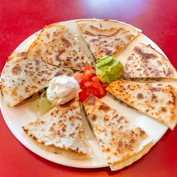 Julio's Mexican Restaurant quesadilla cut into wedges, served with guacamole, diced tomatoes, and sour cream.