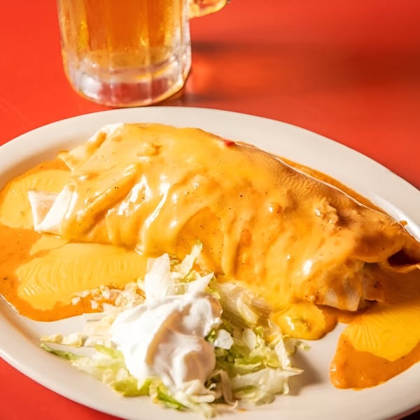 A cheese-covered burrito with shredded lettuce and sour cream, next to a glass of beer.