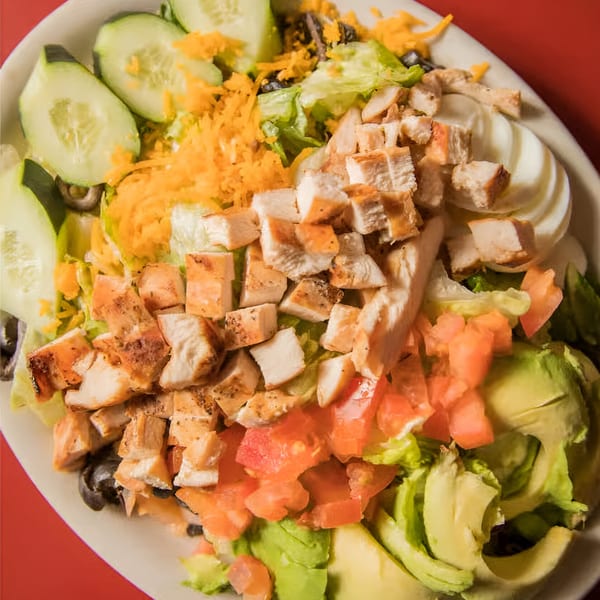 Overhead view of a vibrant salad with grilled chicken, avocado, tomatoes, cucumber, and shredded cheese.