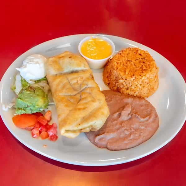 A golden-brown chimichanga with rice, refried beans, guacamole, sour cream, and salsa on a white plate.