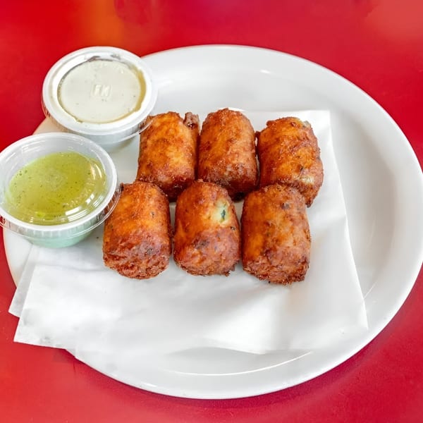 Six golden-brown fried Mexican appetizers with two dipping sauces on a white plate.