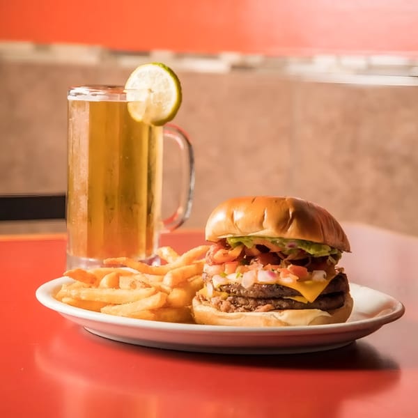 A double cheeseburger with pico de gallo, fries, and a beer with a lime wedge.