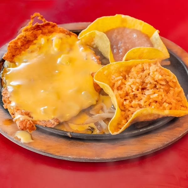 Sizzling fajitas with melted cheese, rice, and refried beans served on a hot plate.