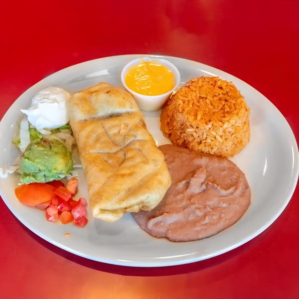 A fried burrito with rice, refried beans, guacamole, sour cream, diced tomatoes, and cheese sauce.