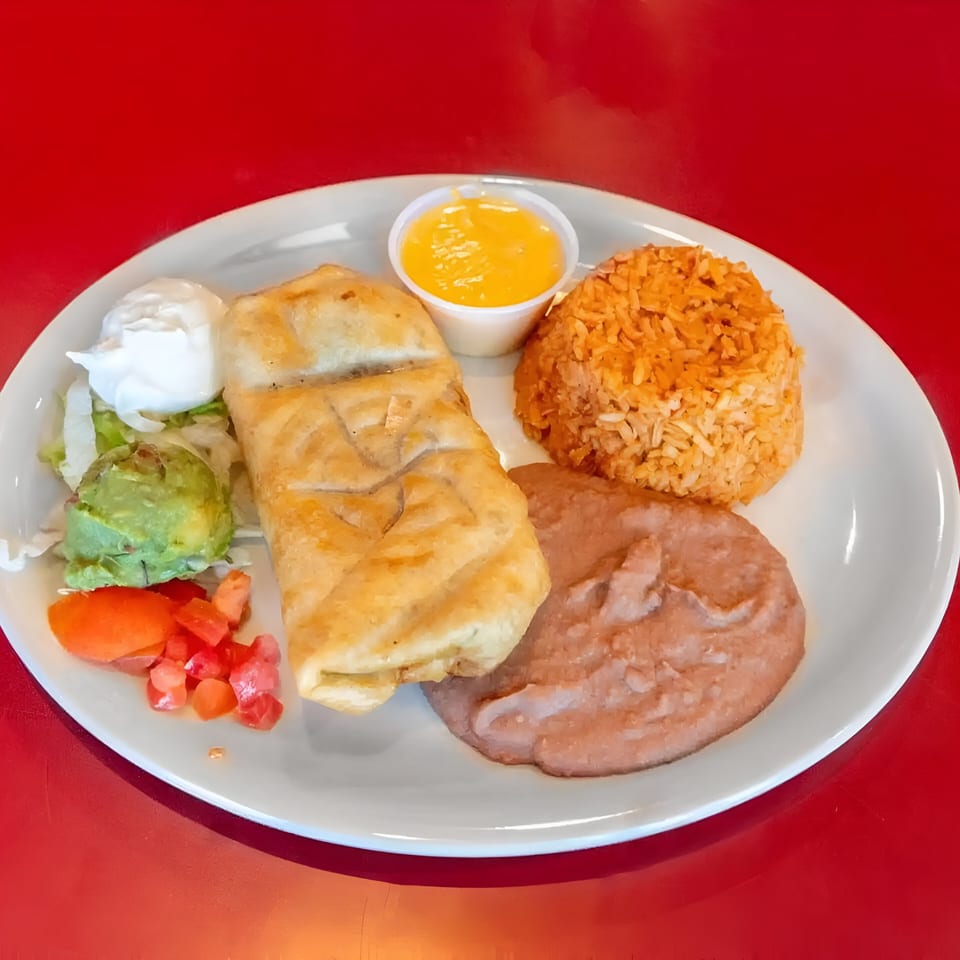 A fried burrito with rice, refried beans, guacamole, sour cream, diced tomatoes, and cheese sauce.